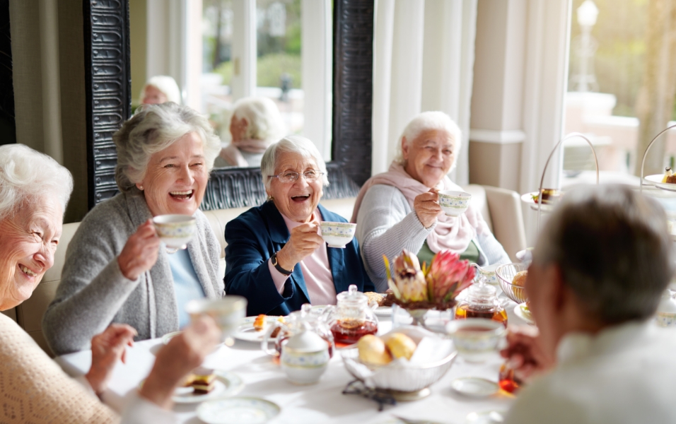 An image of old women laughing and enjoying their tea time.